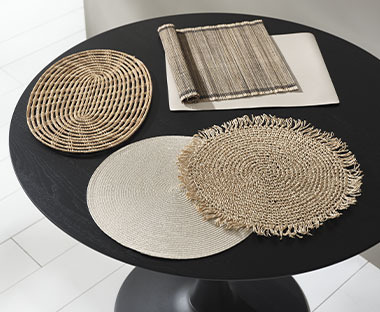 Razne prostirke za stol na površini modernog crnog okruglog stola