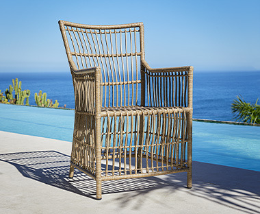 Udobna pletena baštenska stolica na suncu pored bazena