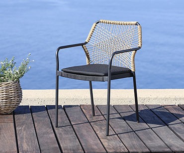 Moderna baštenska stolica metalnog okvira i pletenog naslona za leđa na daskama pored mora