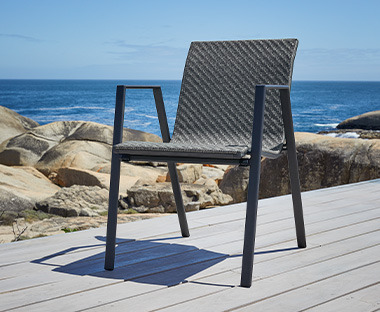 Pletena baštenska stolica crne boje na terasi pored mora