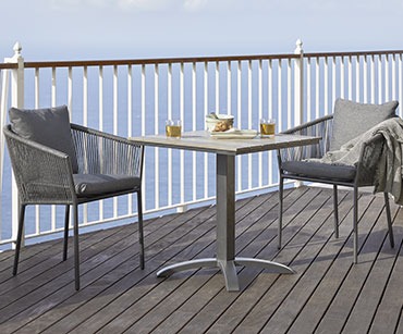 Bistro stol i dvije crne metalne baštenske stolice uz ogradu na balkonu