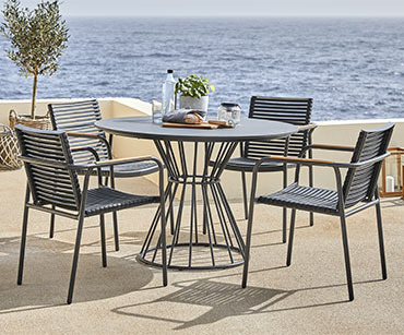 Okrugli stol i crne baštenske stolice uz more na terasi