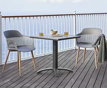 Sivi četvrtasti stol i dvije stolice na terasi uz ogradu pored mora