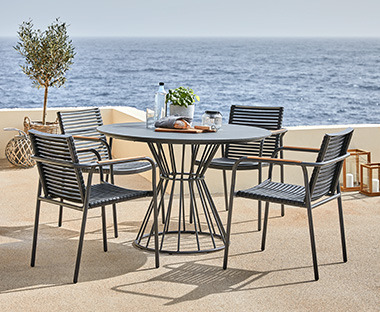Okrugli baštenski stol od metala i lijepe crne baštenske stolice na terasi pored mora