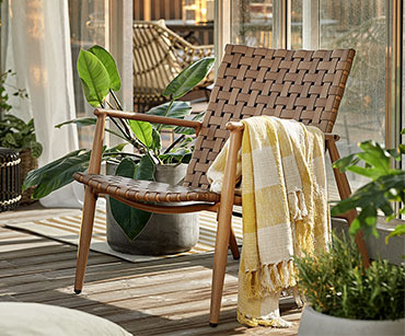 Lijepa pletena lounge stolica na osunčanoj terasi i dekica prebačena preko naslona za ruke
