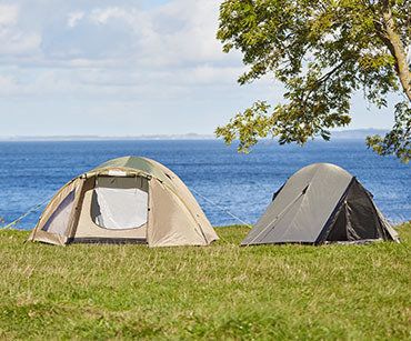 Dva šatora na livadi pored stabla i mora