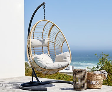 "Jaje-stolica" za ljuljanje sa jastucima za udobnije sjedenje na terasi u blizini mora i korpa i fenjer pored nje