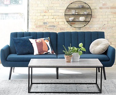 Pravokutni klub stolić sa površinom imitacije betona i tamno plavi moderni kauč