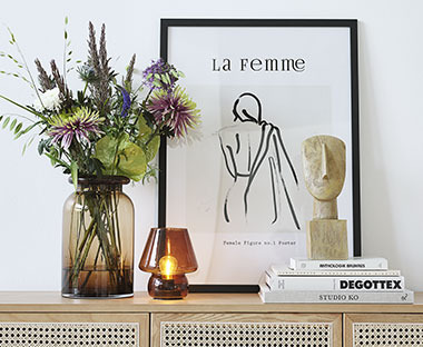 Vaza sa cvijećem, stakleni svijećnjak, okvir za slike, ukrasna statua i knjige na polici uza zid