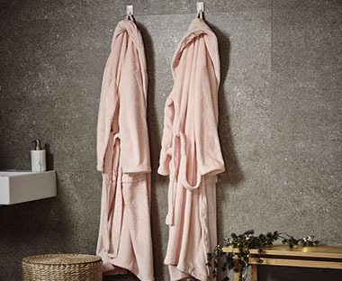 Dva kućna ogrtača roze boje okačeni na zid kupatila