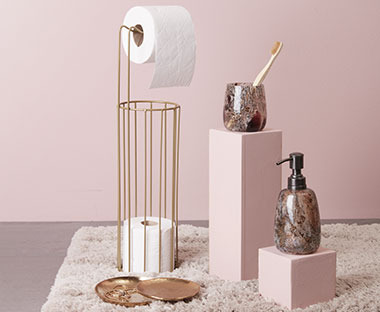Oprema za kupatilo i zlatni držač wc papira pored roze zida