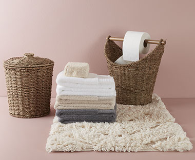 Lijepi bež tepih za kupatilo, dvije pletene korpe i peškiri složeni jedni na druge
