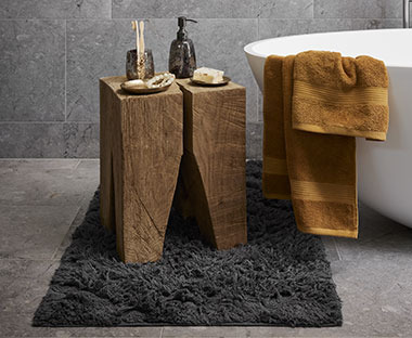 Čupavi tamno sivi tepih za kupatilo, drveni stalak i oprema za kupatilo na njemu