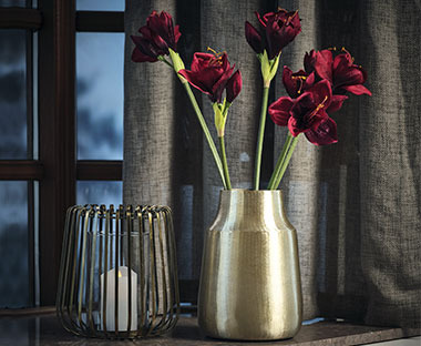 Zlatna vaza sa crvenim umjetnim cvjetovima i elegantni fenjer sa svijećom