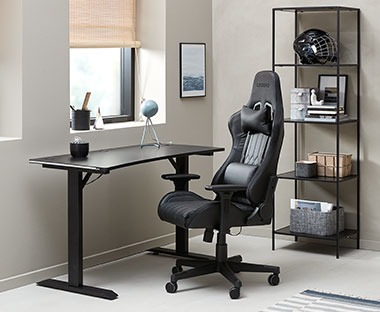 Kvalitetna crna gejmerska stolica i crni metalni radni stol podesive visine u sobi pored prozora