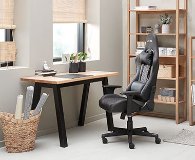 Gaming stolica od crne umjetne kože i moderni mali radni stolić u radnoj sobi pored prozora
