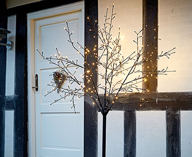 Grane drveta sa LED lampicama u dvorištu pored ulaznih vrata u kuću