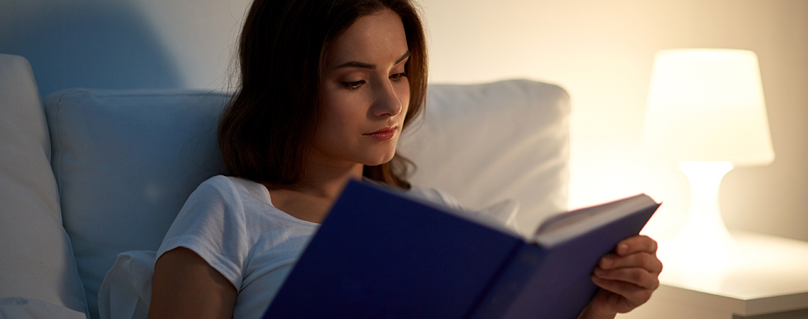 Djevojka u krevetu sa knjigom i pored nje lampa na noćnom ormariću