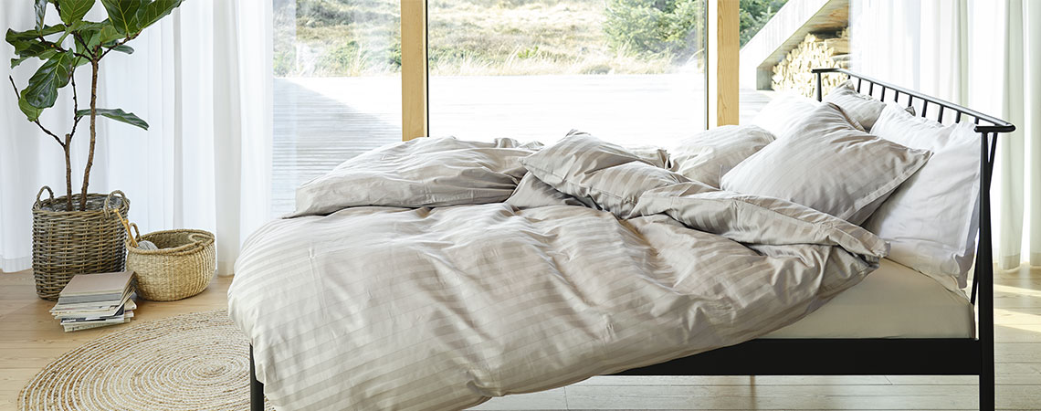 Spavaća soba sa crnim metalnim krevetom, jorganima i jastucima, prekrivena prugastom posteljinom u svjetlo sivoj i bijeloj boji