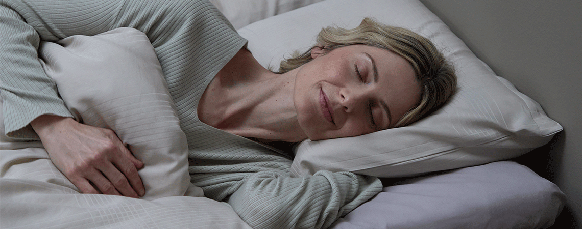 Žena spava na boku u krevetu sa bijelim jastukom i jorganom
