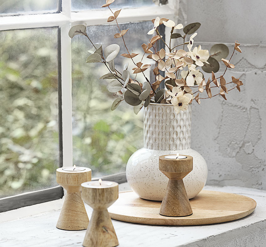 Svijetlo-bež ili bijela reljefna vaza sa umjetnim cvijećem i drvenim svijećnjacima