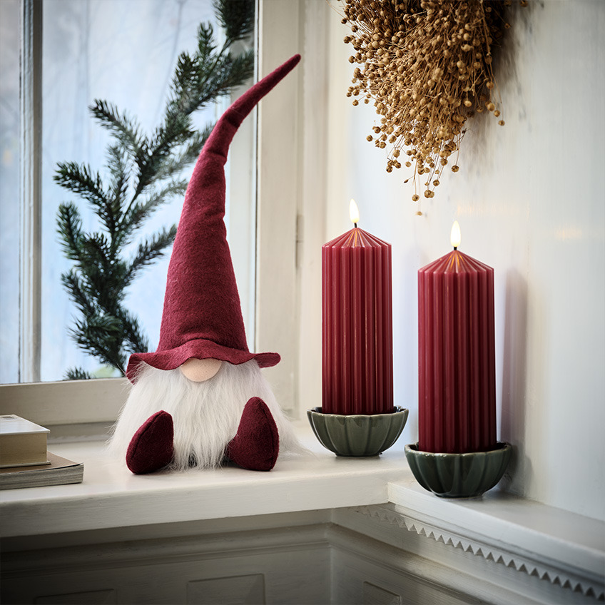 Skandinavski božićni patuljak na prozorskoj dasci pored velikih crvenih svijeća
