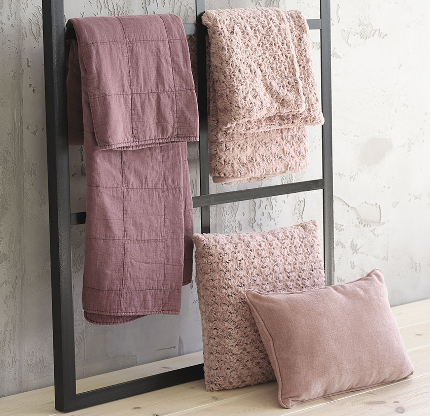 Dvije deke i dva ukrasna jastuka u rozim nijansama na okviru uz zid