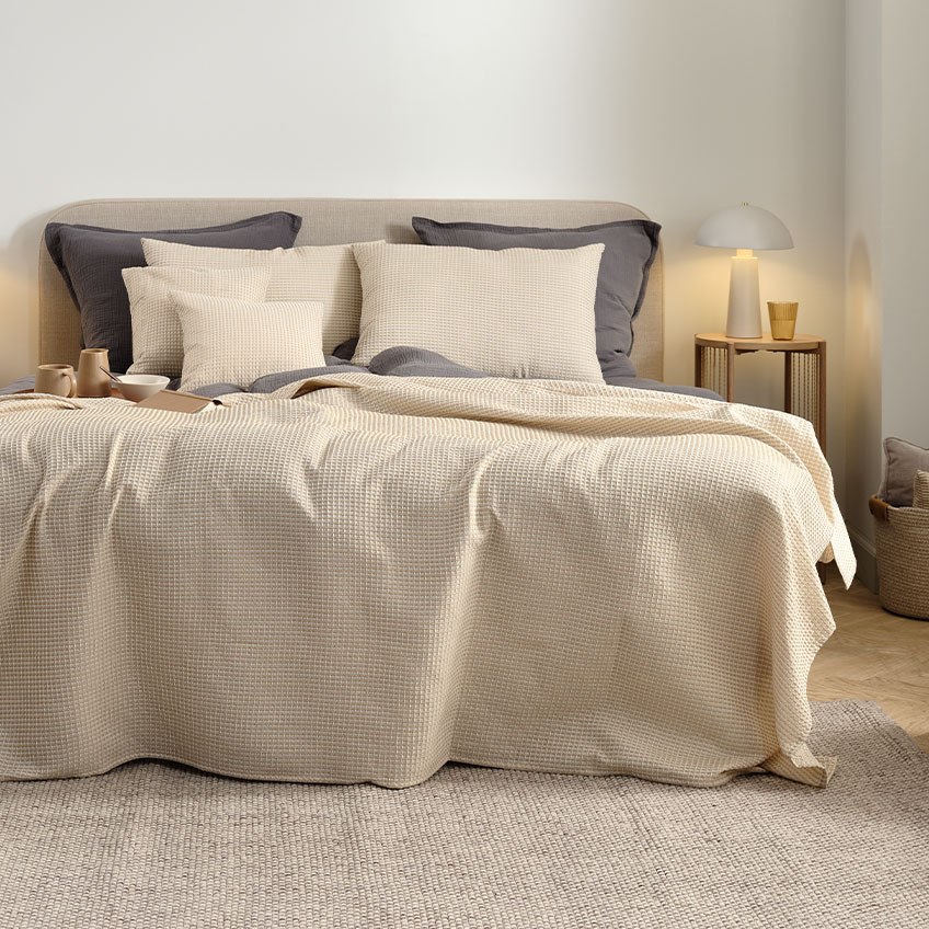Prekrivač za krevet, jastuci za leđa i ukrasni jastuci u toploj bež boji na bračnom krevetu u spavaćoj sobi