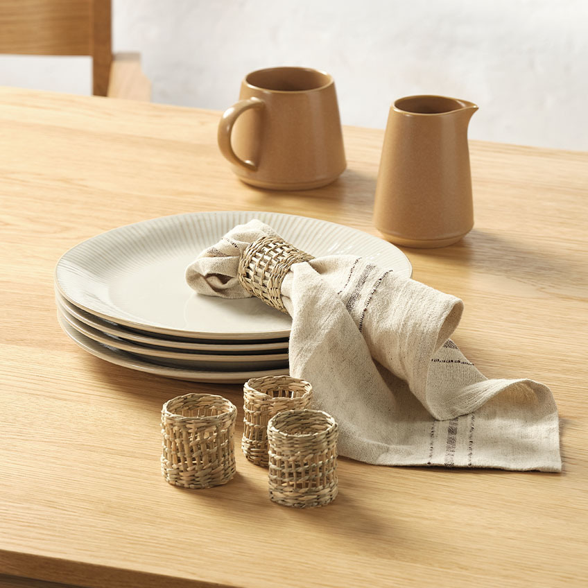 Bijeli tanjiri sa teksturom, bokal za mlijeko, platnena salveta i držači za salvete na trpezarijskom stolu