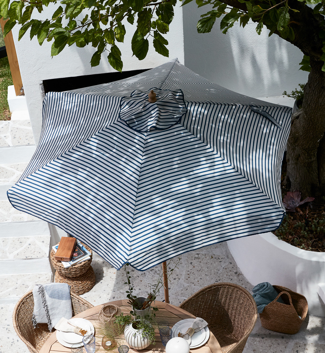 Prugasto bijelo-plavi suncobran na terasi iznad baštenskog stola i stolica