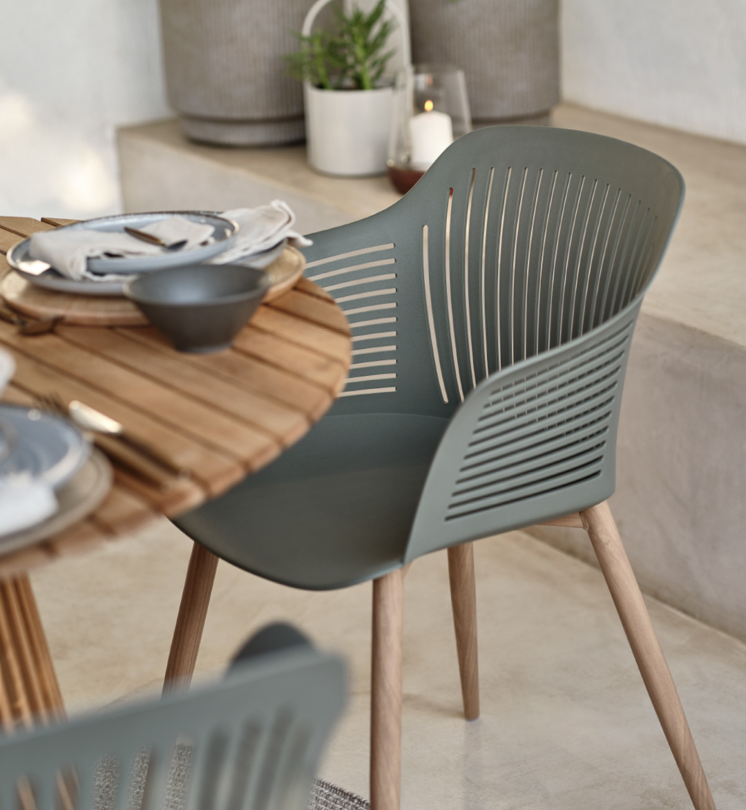 Lijepa siva baštenska stolica sa sjedalom od polipropilen i nogama od čelika na terasi uz stol od tikovine