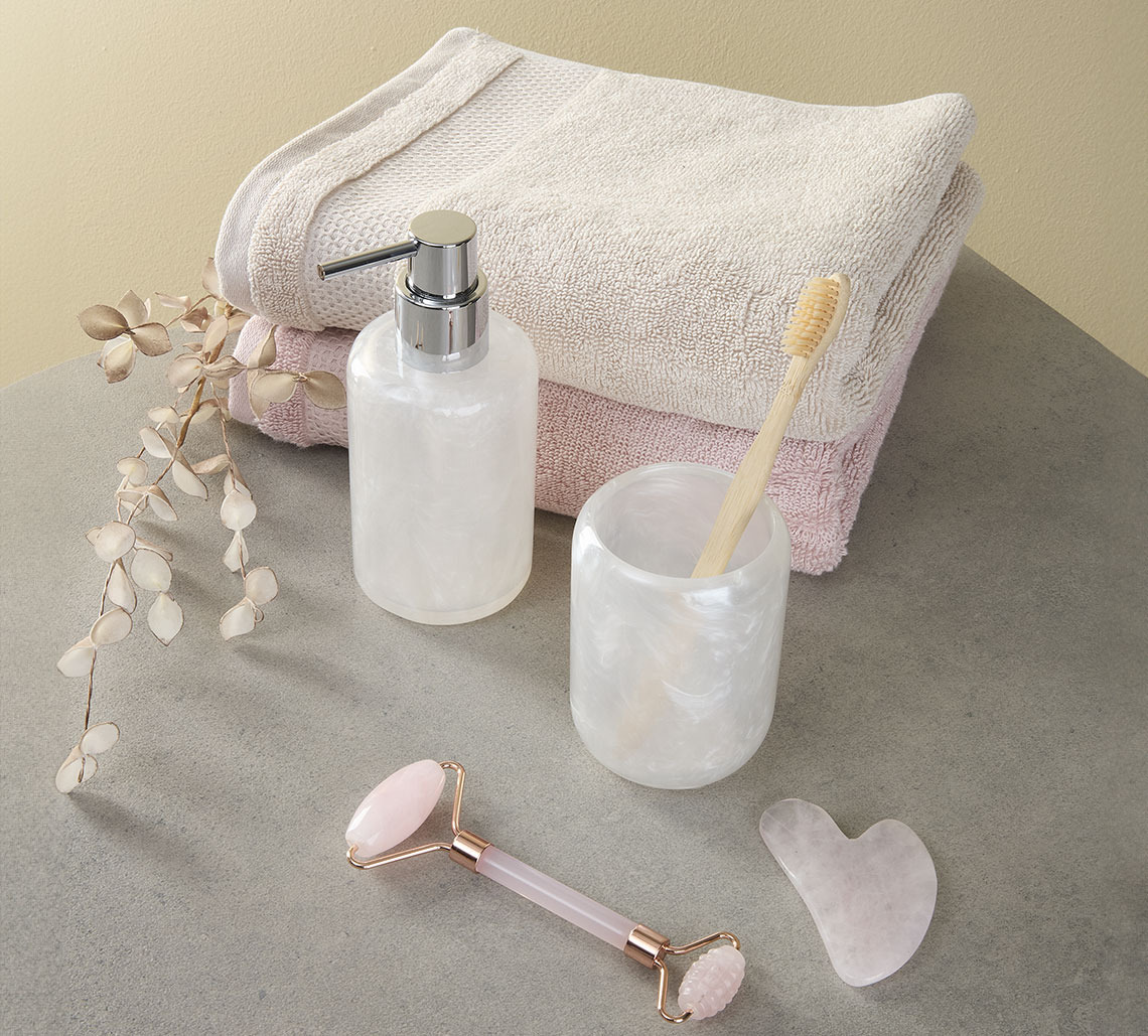 Peškir boje pijeska i roze peškiri pored držača četkice za zube, dozera tekućeg sapuna i valjak za lice i masažnog kamena