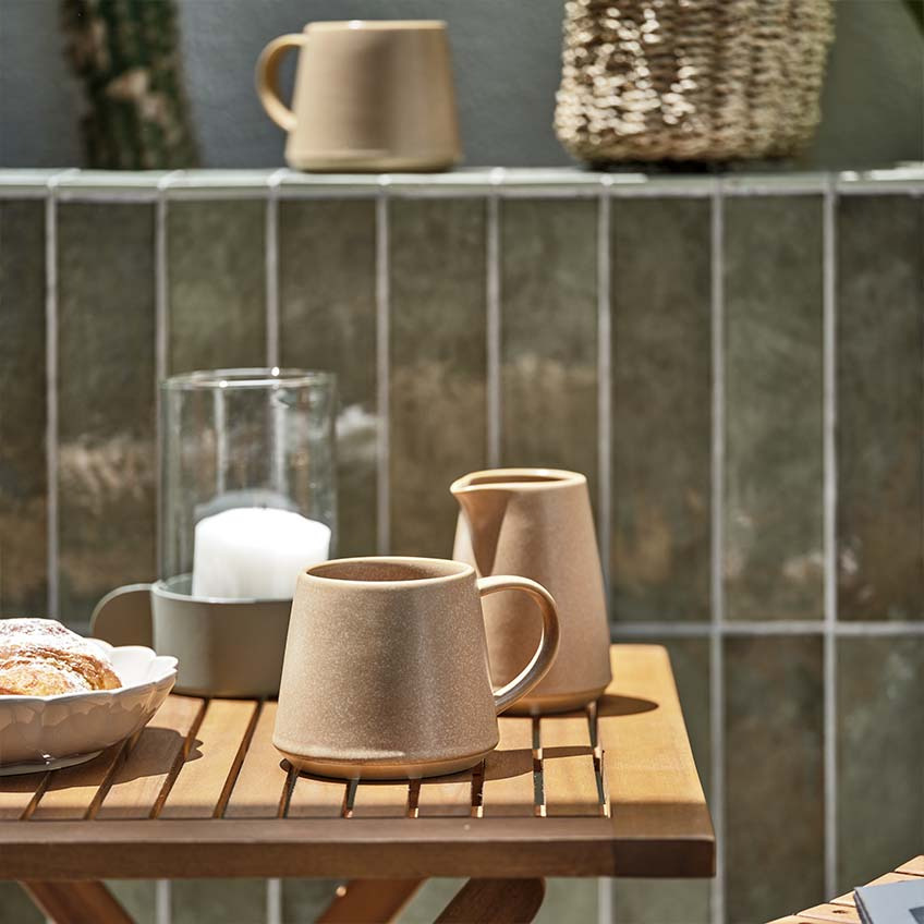 Šolja za kafu i bokalčić za mlijeko na malom drvenom baštenskom stolu