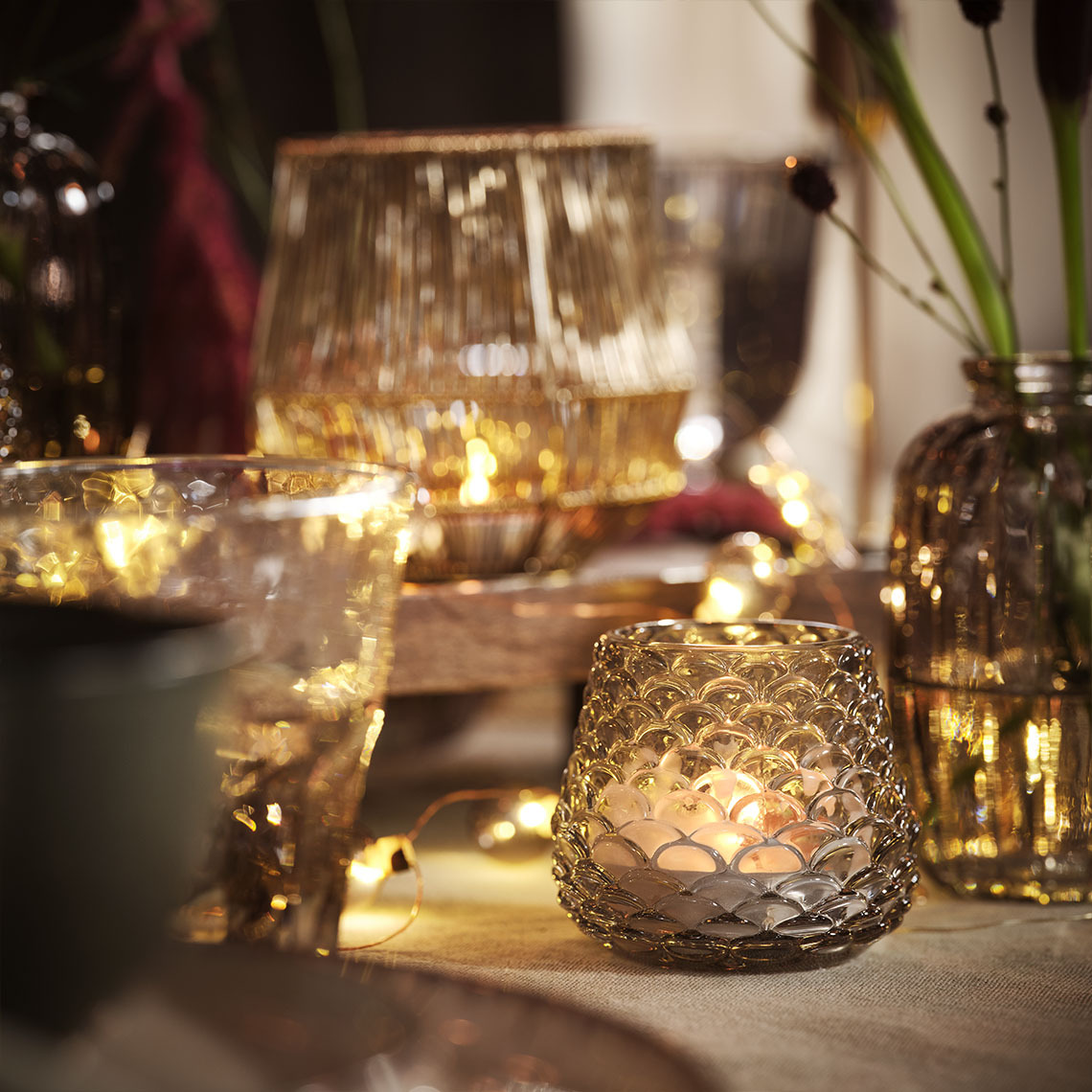 Blagovaonski stol osvijetljen svijećama i čajnim svjećicama u držačima za čajne svjećice i svjetiljkama u nizu