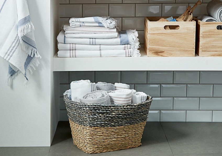 Kupatilski peškiri na polici pored drvenih sanduka za odlaganje i jedna pletena torba