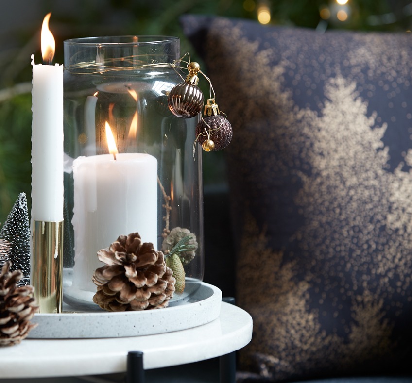 Vaza sa svijećom na stoliću pored ukrasnog jastuka s novogodišnjim motivima