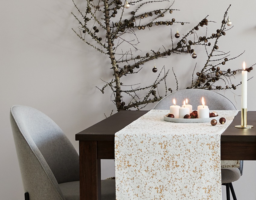 Novogodišnji nadstolnjak bijele boje sa zlatnim detaljima na stolu od masivnog tamnog drveta