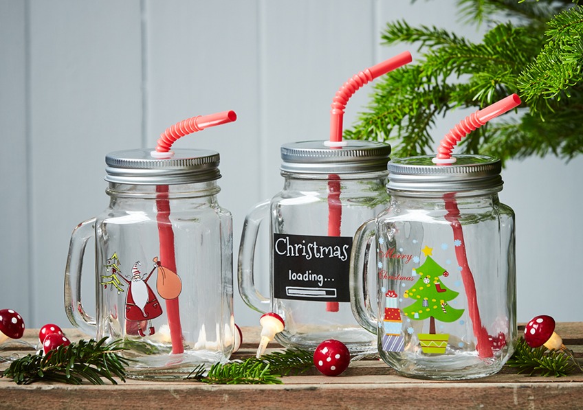 Staklena čaša sa ručkicom, poklopcom i slamkom ukrašena novogodišnjim sličicama