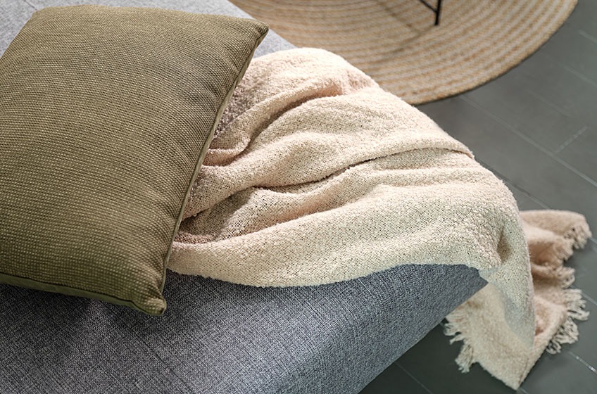 Zeleni ukrasni jastuk i deka boje pijeska na sivom kauču