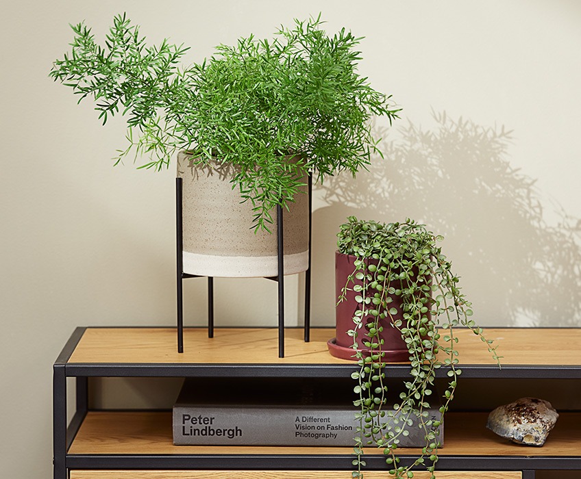 Umjetne biljke na modernoj TV polici, jedna biljka stoji uspravno, a druga visi 