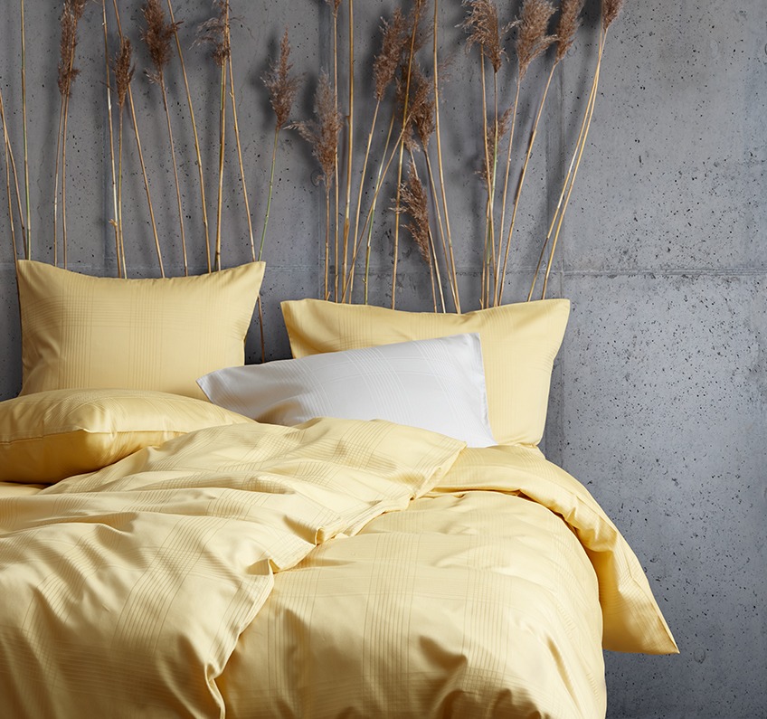 Žuta posteljina izrađena od 51% recikliranih poliesterskih vlakana i 49% pamučnog satena u spavaćoj sobi sa betonskim zidovima