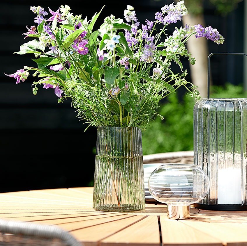 Staklena vaza i fenjeri na okruglom baštenskom stolu