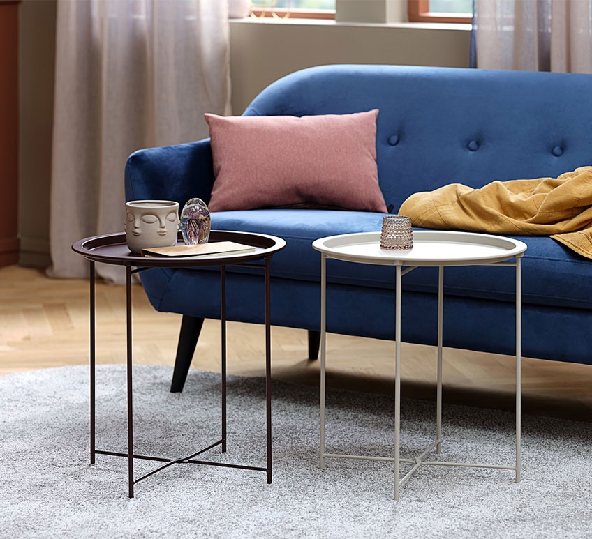 Dva okrugla metalna stolića ispred tamno plavog modernog kauča u dnevnoj sobi