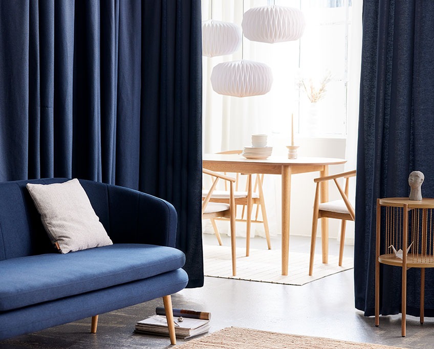 Plave zavjese iza sofe razdvajaju dnevnu sobu od trpezarije
