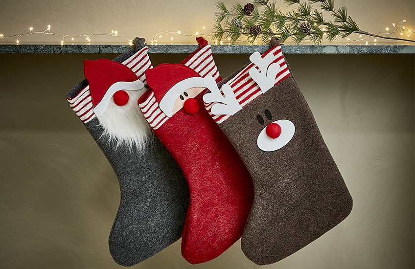 Novogodišnje čarape vise sa police sa tematikom Deda Mraza, patuljka, i irvasa