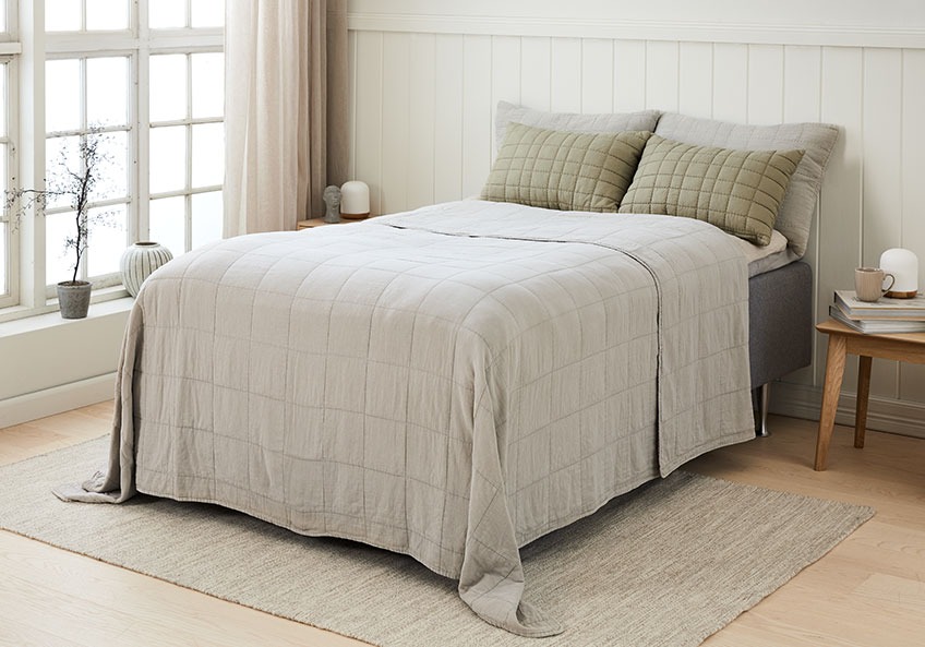 Krevet sa štepanom dekom i odgovarajućim jastucima za leđa u svjetloj spavaćoj sobi