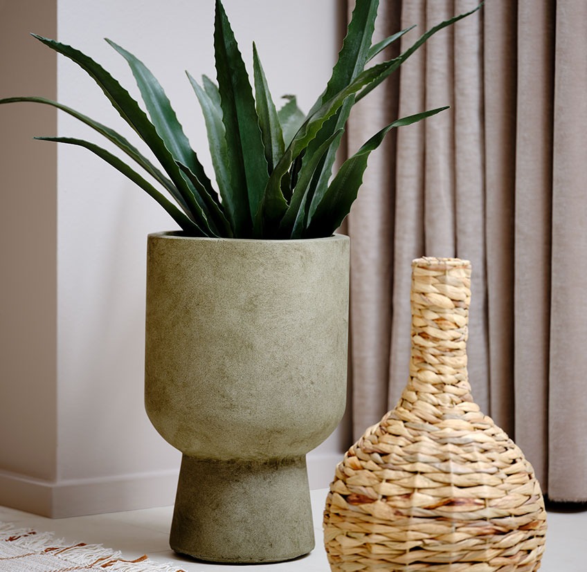 Zelena saksija sa umjetnom biljkom pored pletene vaze 