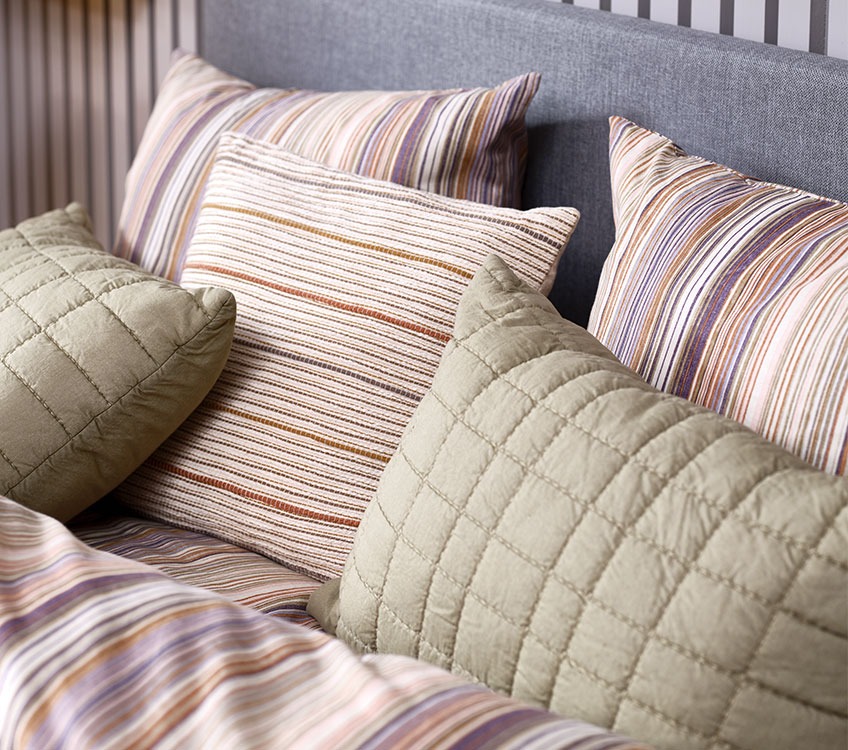 Prugasta posteljina sa ukrasnim jastukom i zelenim jastukom za leđa