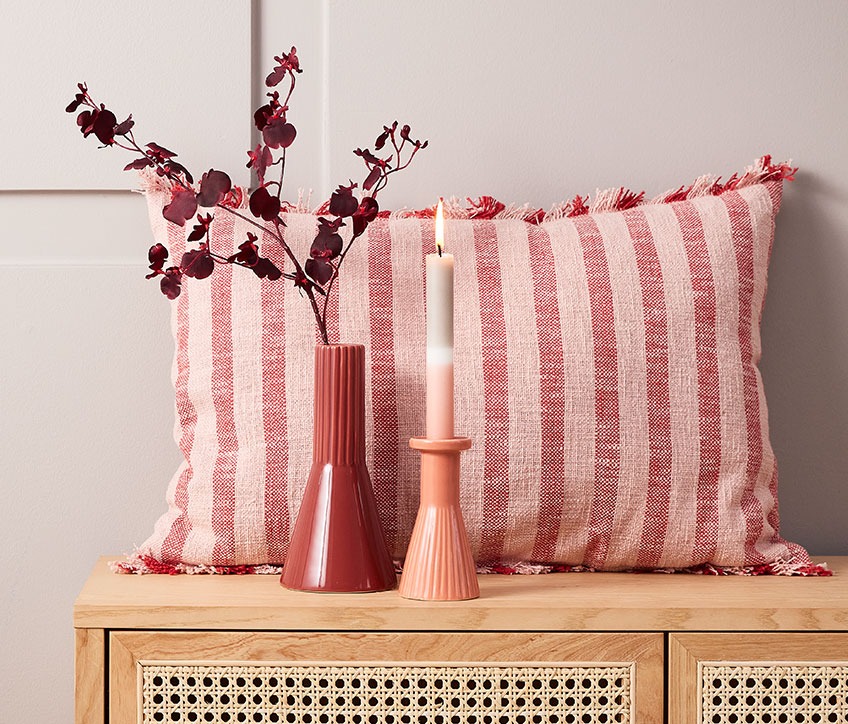 Ukrasni prugasti jastuk iza crvene vaze i svijećnjaka sa prugastom svijećom