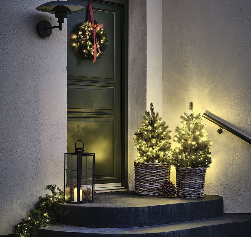 Two lights trees in front of front door and Christmas wreath with red bow